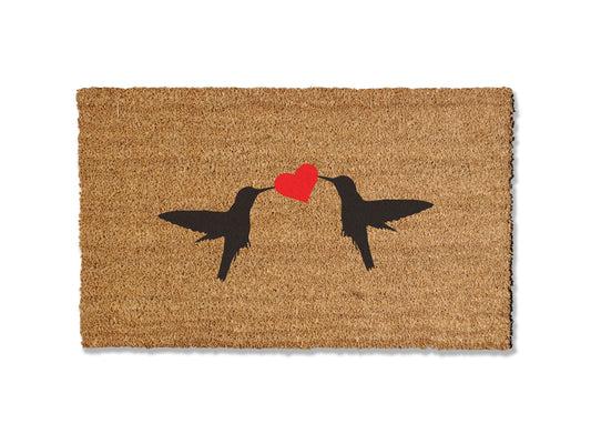 Enhance your entryway with our 1/2-inch thick coir doormat adorned with two hummingbirds and a heart in the middle. Available in multiple sizes, this charming mat not only adds a touch of nature to your doorstep but is also highly effective at trapping dirt. 